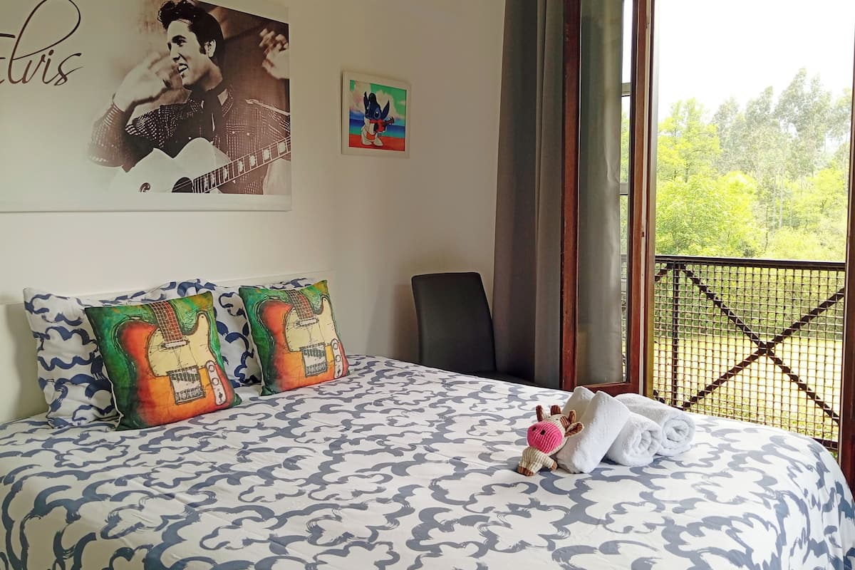 A bedroom with a bed, pillows, a chair, and a window with a view of trees.