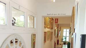 A hallway with artwork on the walls, a white bench, and a wooden floor. - Prau Riu (Llanes)