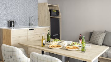 Una cocina compacta equipada con microondas, lavamanos y un refrigerador pequeño. Se aprecia una mesa de comedor con platos de comida, botellas y una tetera.