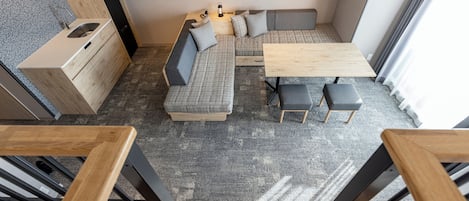 Un espacio habitable moderno y funcional con kitchenette, sofá, mesa de comedor y escalera.
