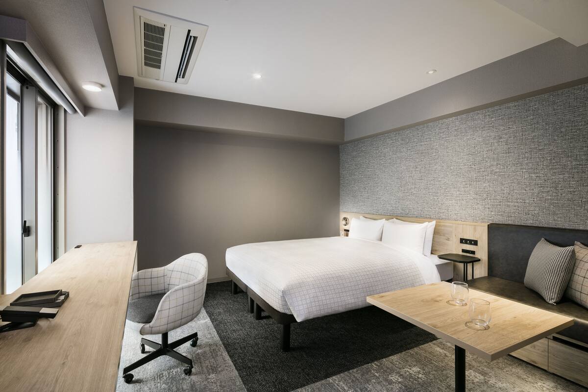 A modern hotel room with a large bed, a desk, a chair, and a small table.