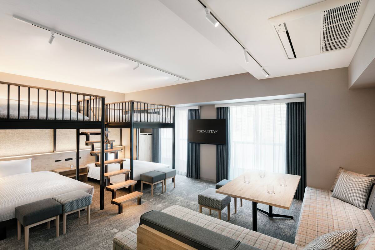 A modern hotel room with a bunk bed, a desk, and a seating area.