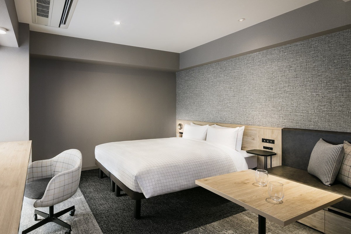 Une chambre d’hôtel moderne équipée d’un lit, d’un bureau, d’une chaise et d’une petite table avec un verre.