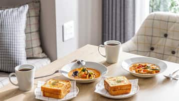 A dining table with two bowls of soup, two cups of coffee, and two plates of toast.