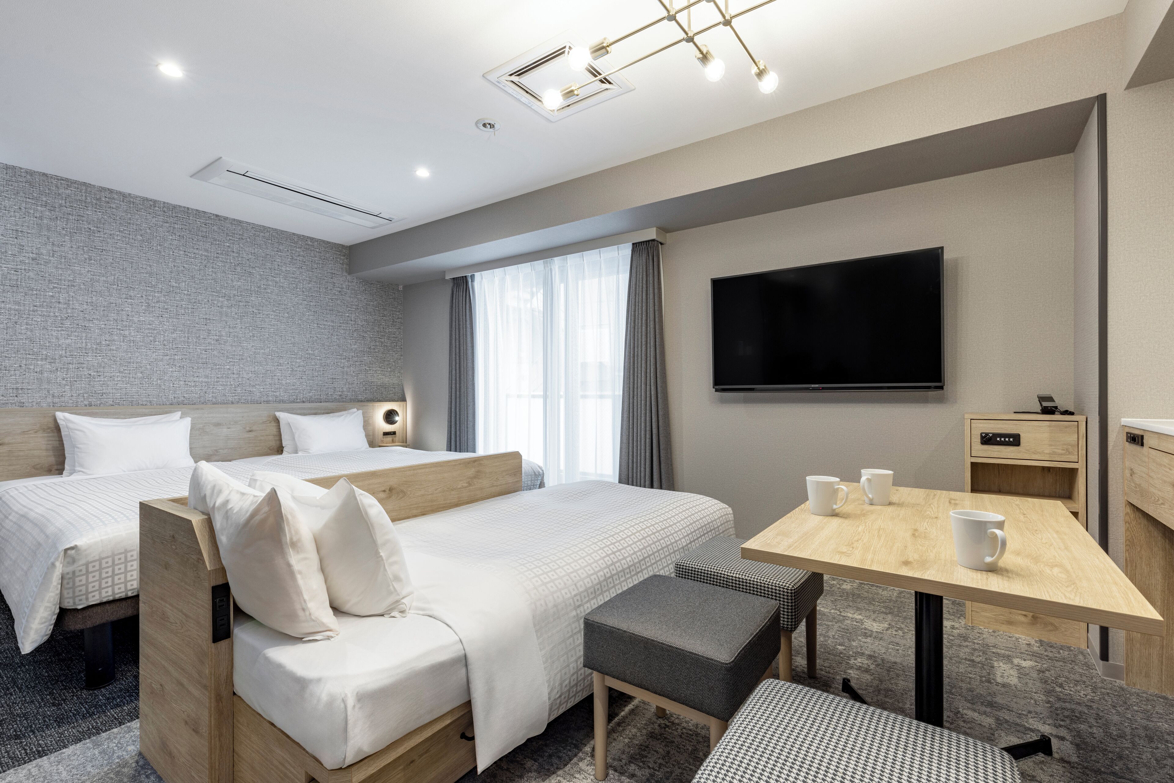 A modern hotel room with two beds, a flat-screen TV, a wooden desk, and a small seating area.