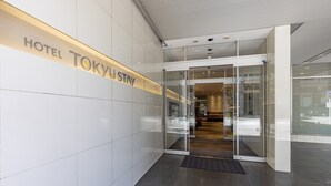 Une entrée d’hôtel moderne avec une porte en verre et une enseigne indiquant « HÔTEL TOKYU STAY ».
