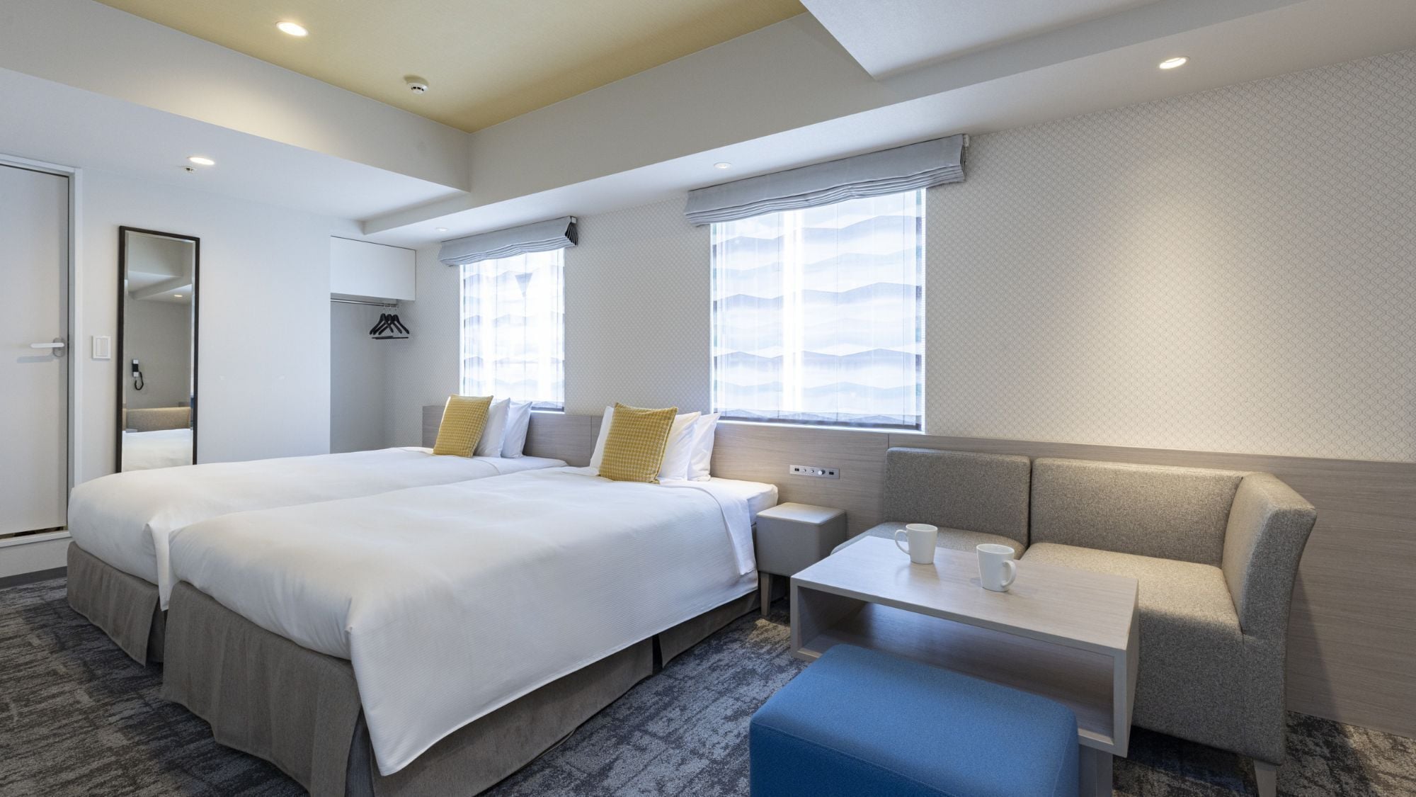 Een hotelkamer met een groot bed, een kleine tafel met twee kopjes, een bank en een grote spiegel.
