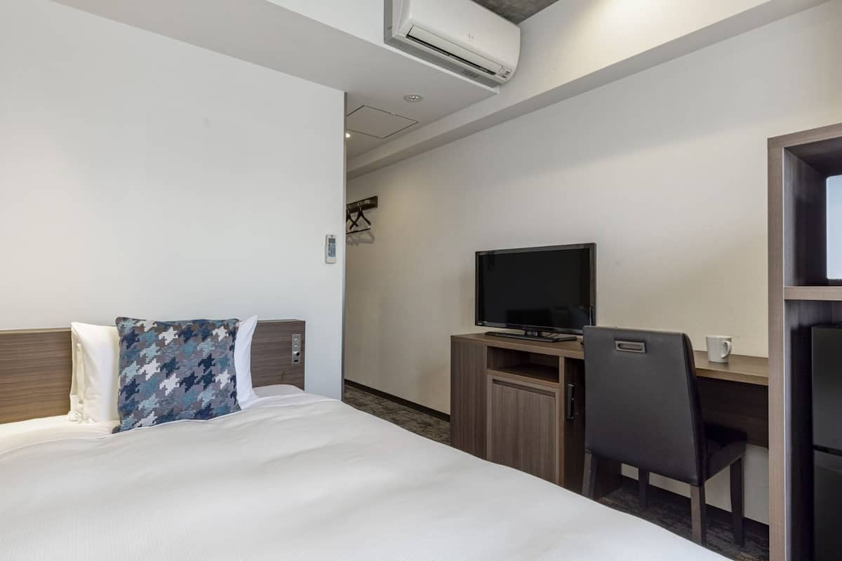 Hotellihuone, jossa on sänky, työpöytä, jossa on televisio, tuoli ja mikroaaltouuni.