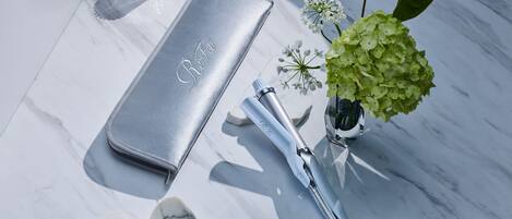 A marble surface with a silver case, a hairbrush, a vase with flowers, and a candle.