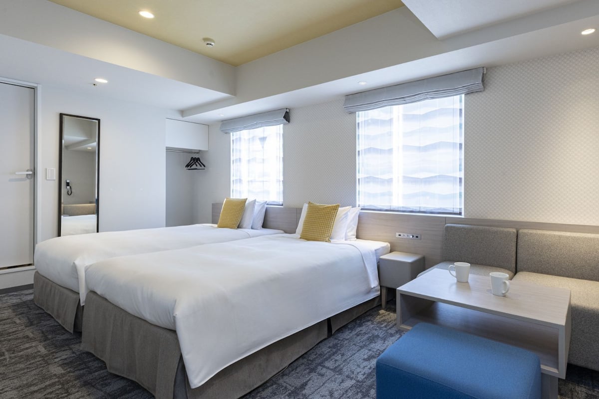 A hotel room with two beds, a seating area, a small table, and a window.