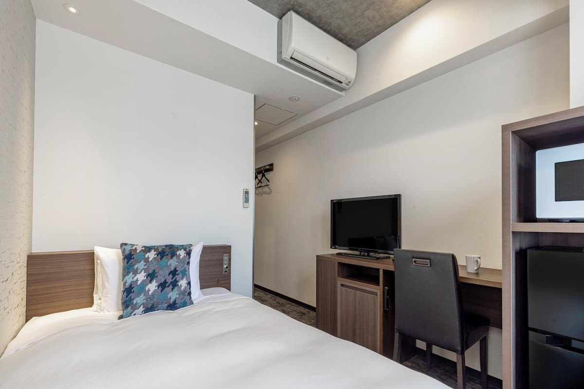 A hotel room with a bed, a desk with a computer, a TV, and an air conditioning unit.
