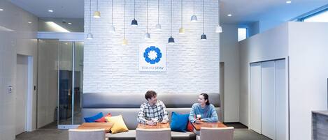 A modern lobby with a white brick wall, a logo, and a seating area with tables and chairs.