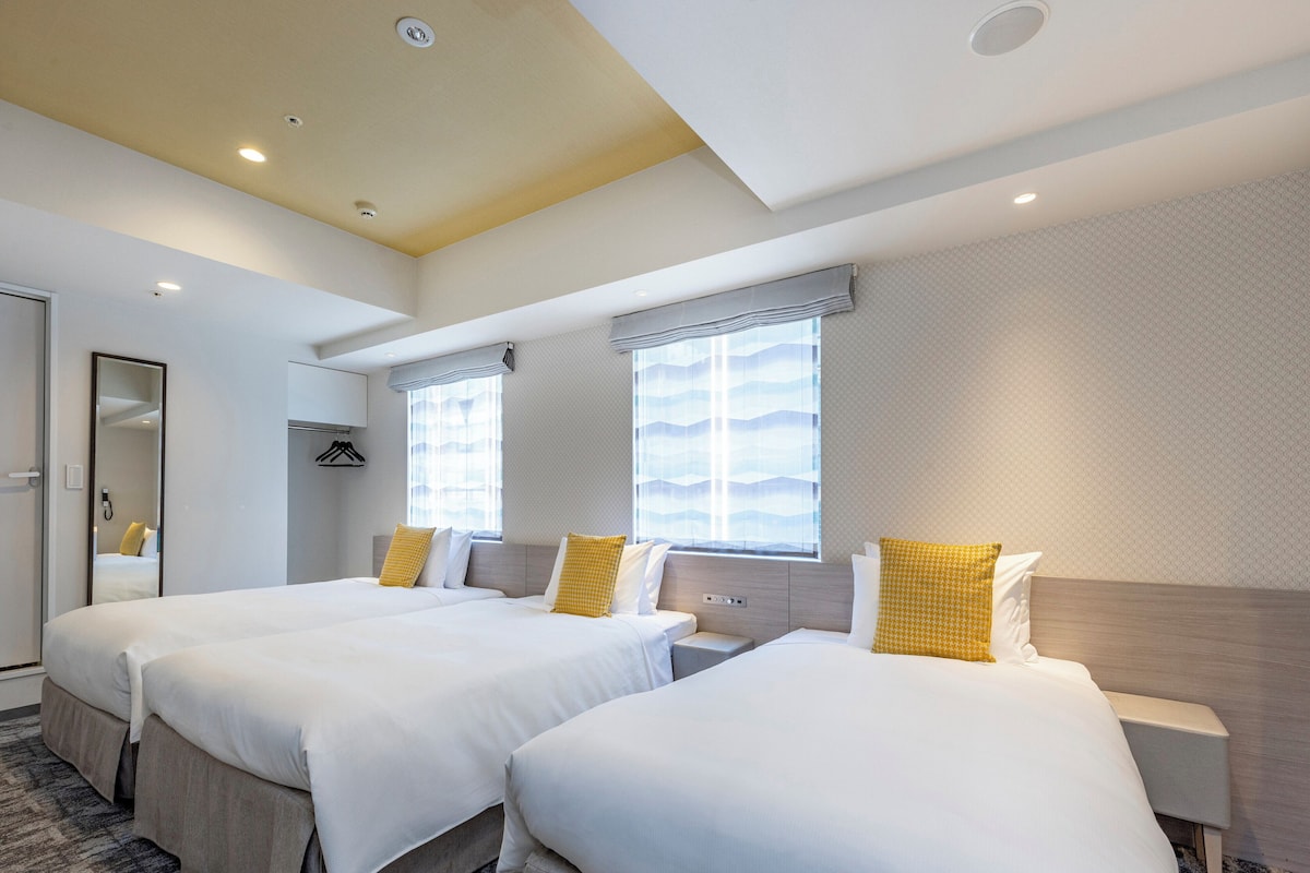 A hotel room with two beds, a mirror, a bedside table, and a window with a view.