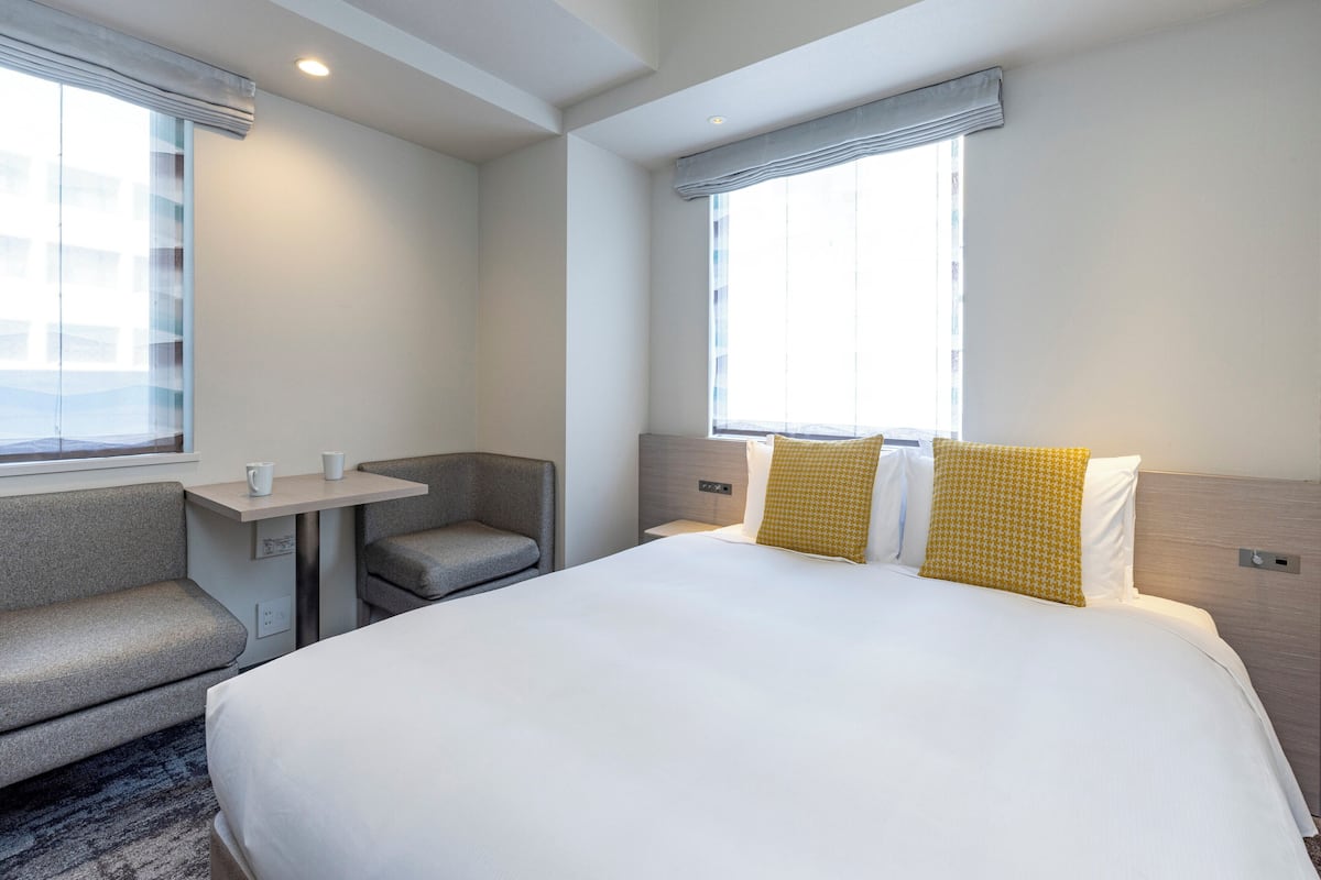 A hotel room with a bed, a small table, a chair, and a window.