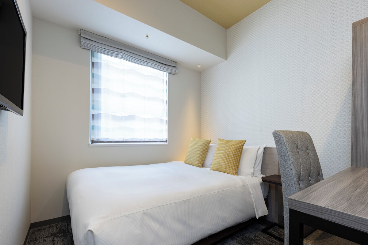 A hotel room with a bed, a table, and a chair.