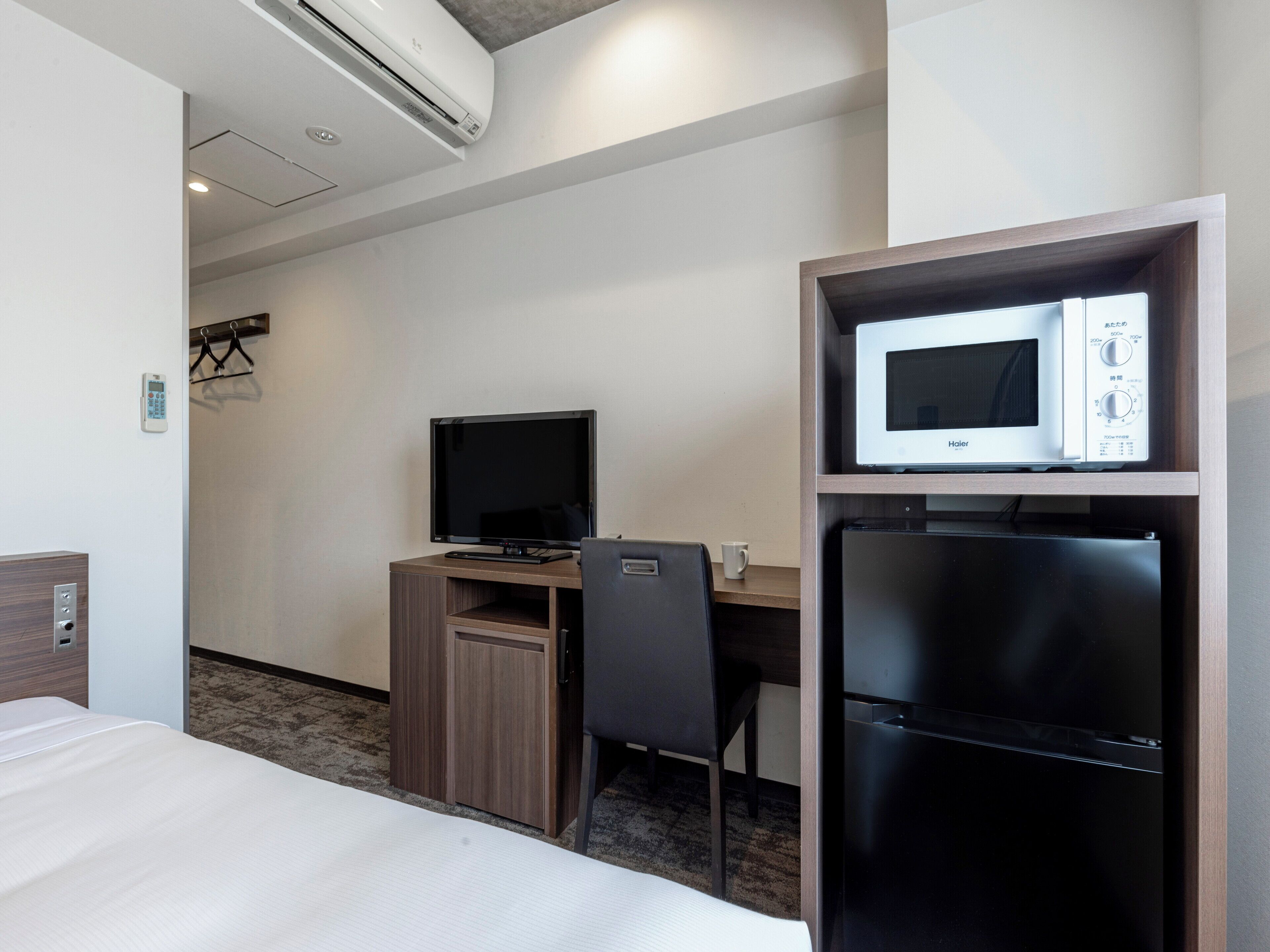 Een hotelkamer met een bed, een bureau met een computer, een magnetron en een koelkast.