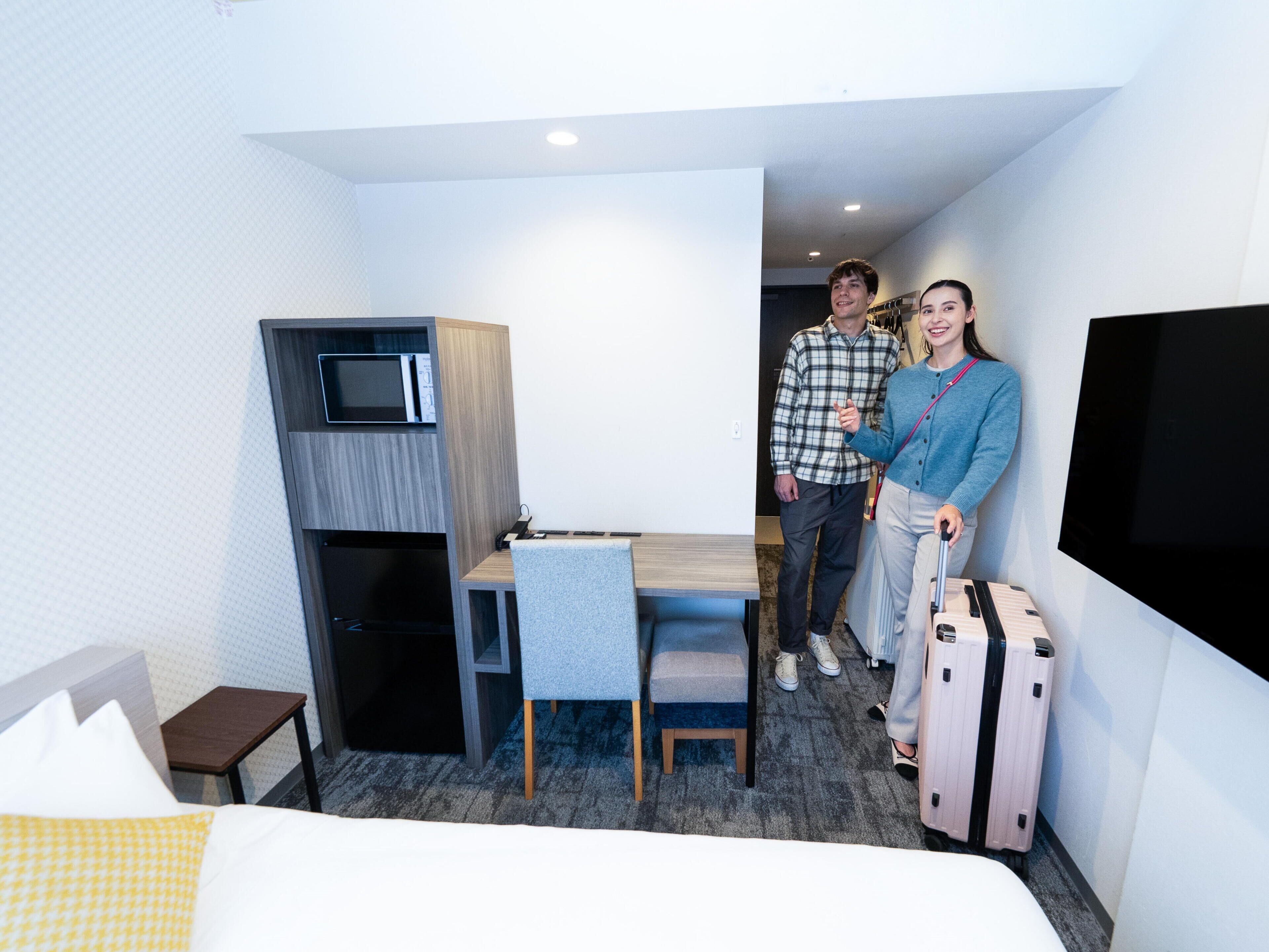 Ein Hotelzimmer mit Bett, Schreibtisch mit Stuhl, Mikrowelle, Fernseher und Koffer.