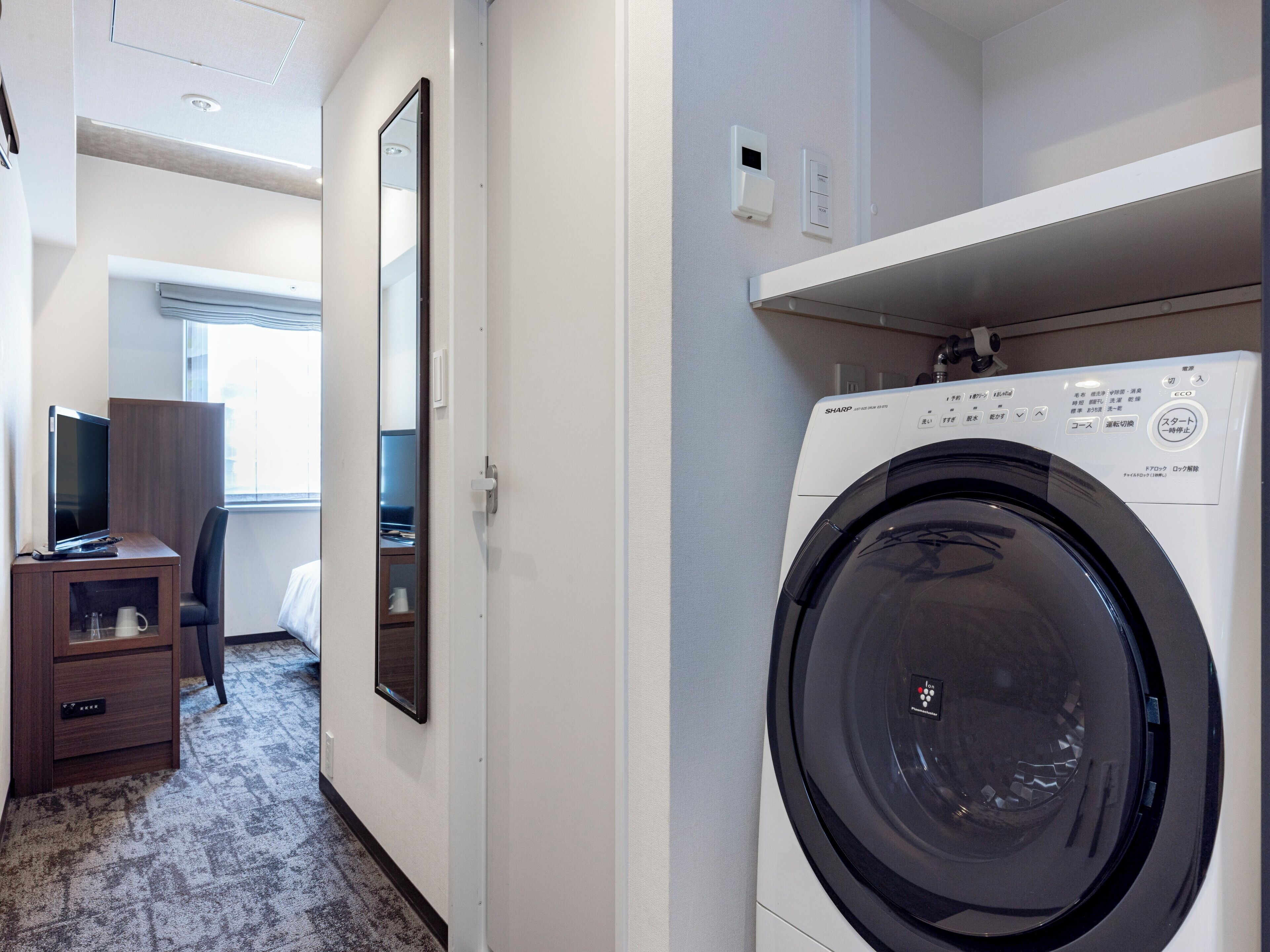 Una habitación de hotel con lavadora, televisor, escritorio y silla.