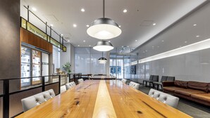 Une salle de conférence avec une longue table en bois, des chaises blanches, un canapé en cuir marron et des luminaires suspendus.
