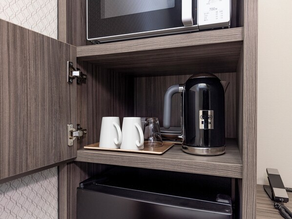 Un coin cuisine équipé d’un four à micro-ondes, d’une machine à café et de deux tasses sur un plateau.
