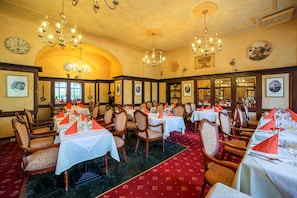 Un comedor elegante con varias mesas, sillas, candelabros y cuadros en las paredes.