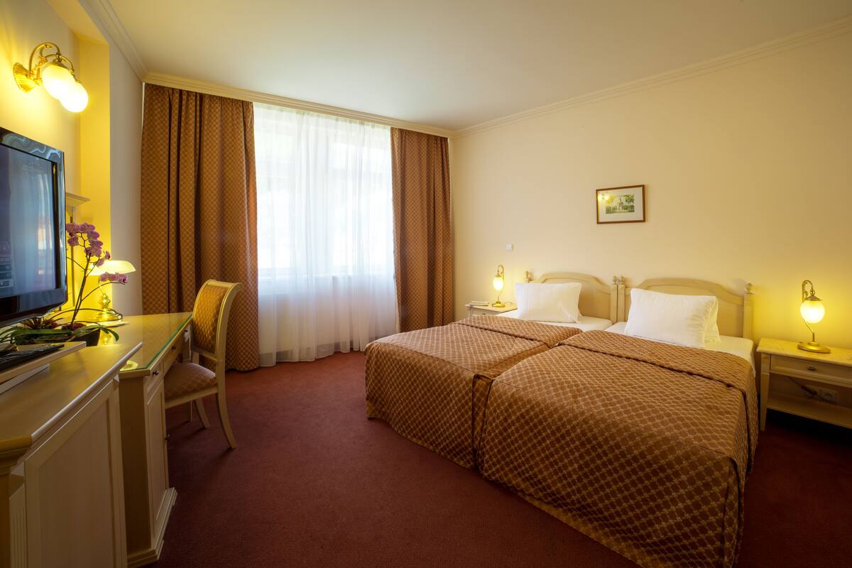 A hotel room with a bed, a desk, a chair, a television, and a window with curtains.