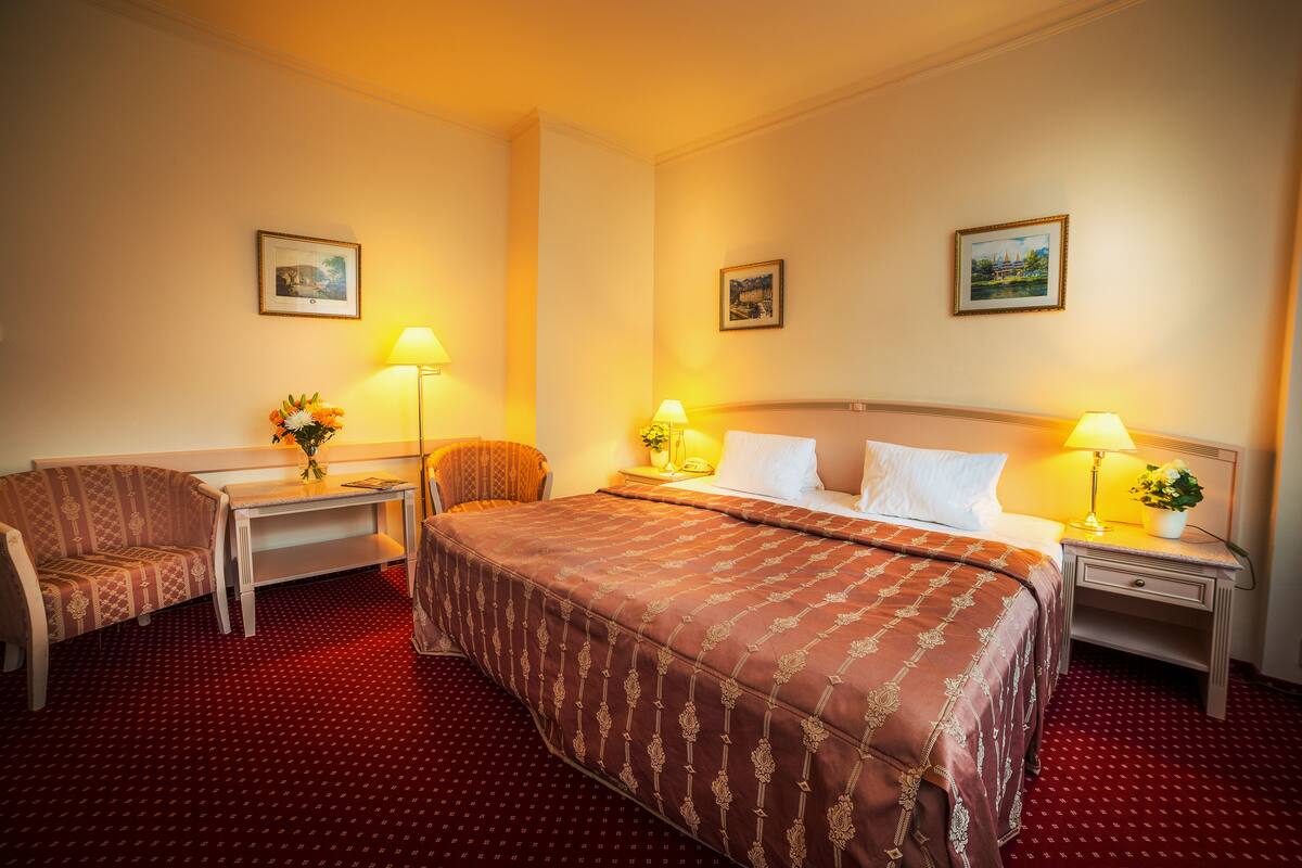 A hotel room with a large bed, two bedside tables with lamps, a chair, and a desk.