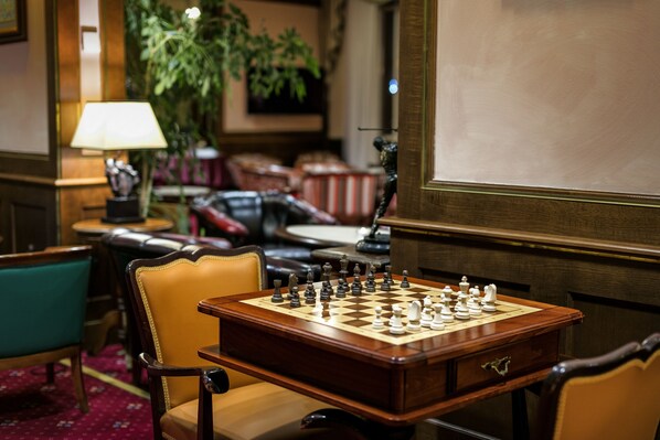 A chessboard set on a wooden table in a room with leather chairs and a lamp.