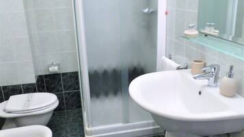 Ein Badezimmer mit Dusche, zwei Toiletten, einem Waschbecken und einem Spiegel.