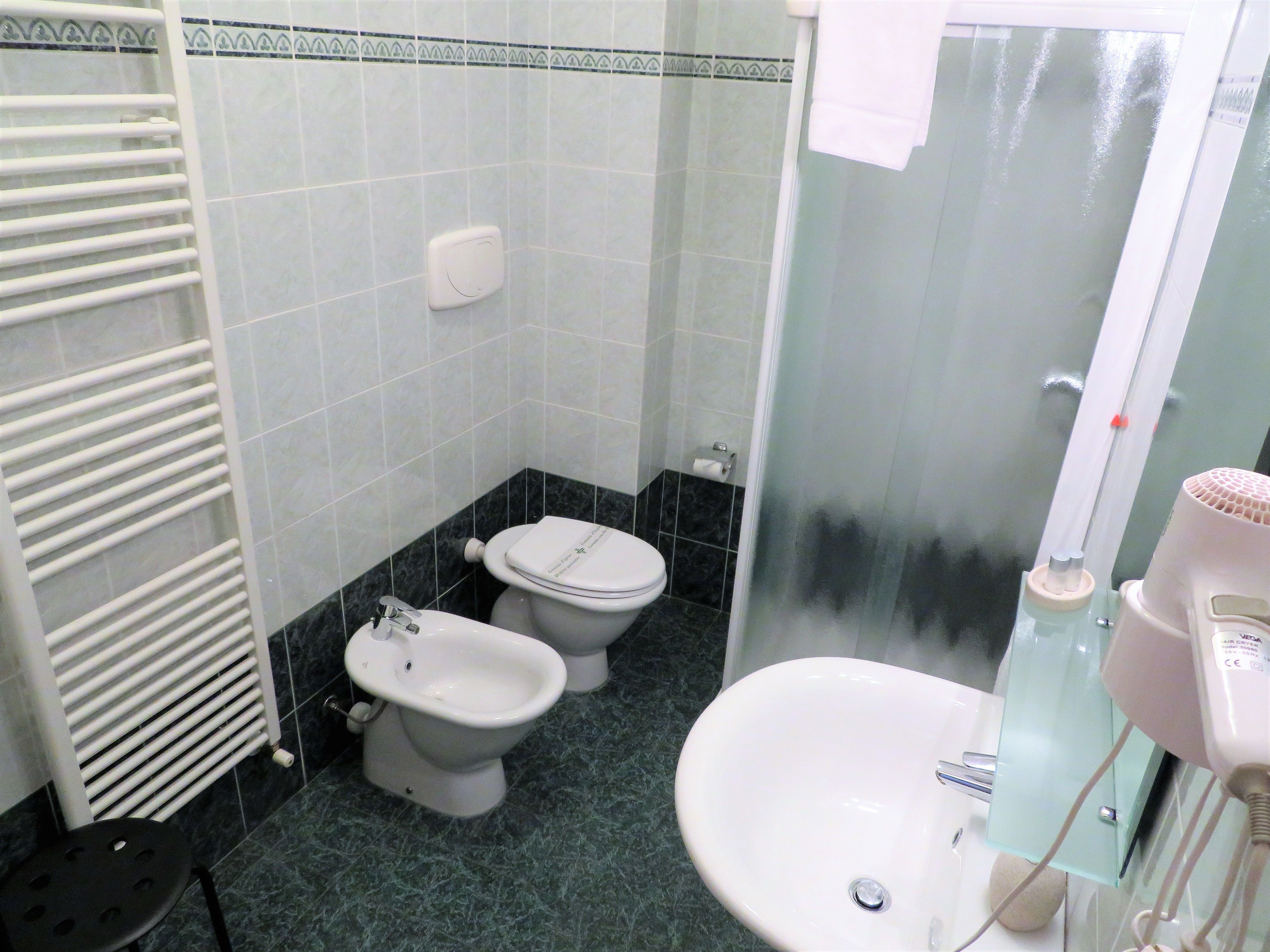 A bathroom with two toilets, a sink, a glass shower enclosure, and a towel rack.