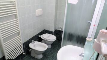 A bathroom with two toilets, a sink, a glass shower enclosure, and a towel rack.