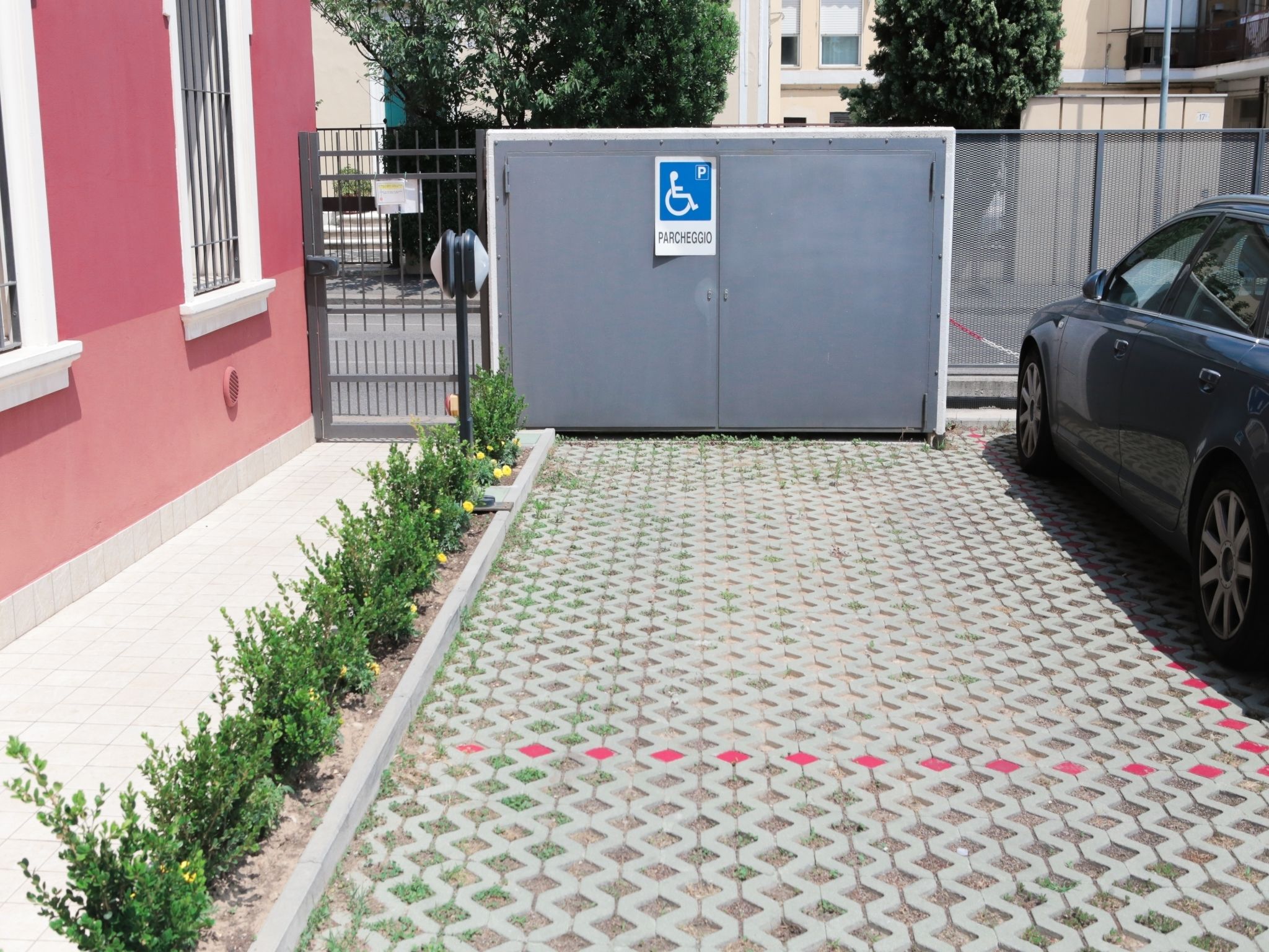 Ein Parkplatz mit Parkplatz für Behinderte-Kennzeichnung, einem Auto und einem Gebäude mit roter Wand und Tor.