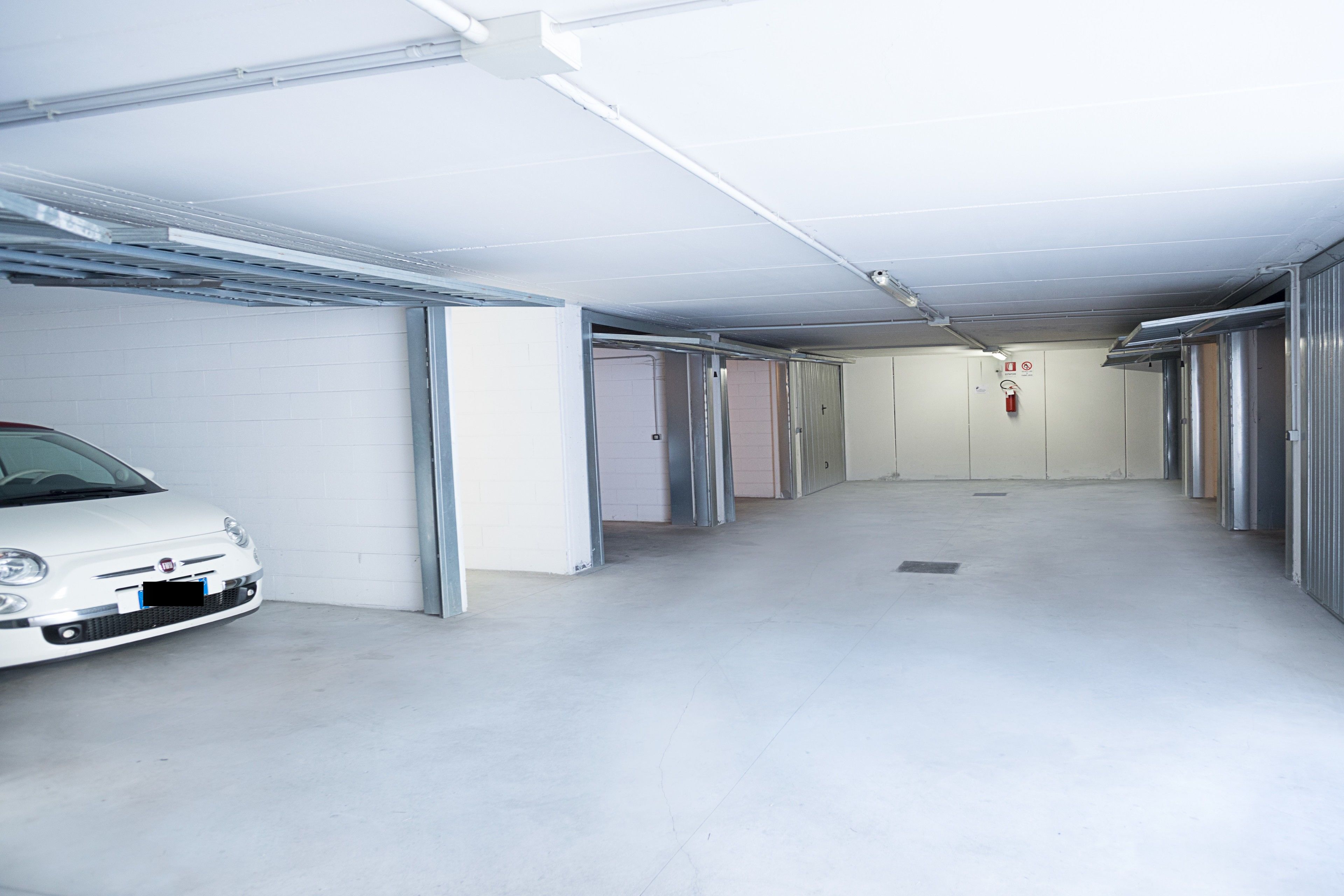 A clean, empty hallway with a white car parked on the left. There are closed doors on both sides and a fire extinguisher mounted on the wall.