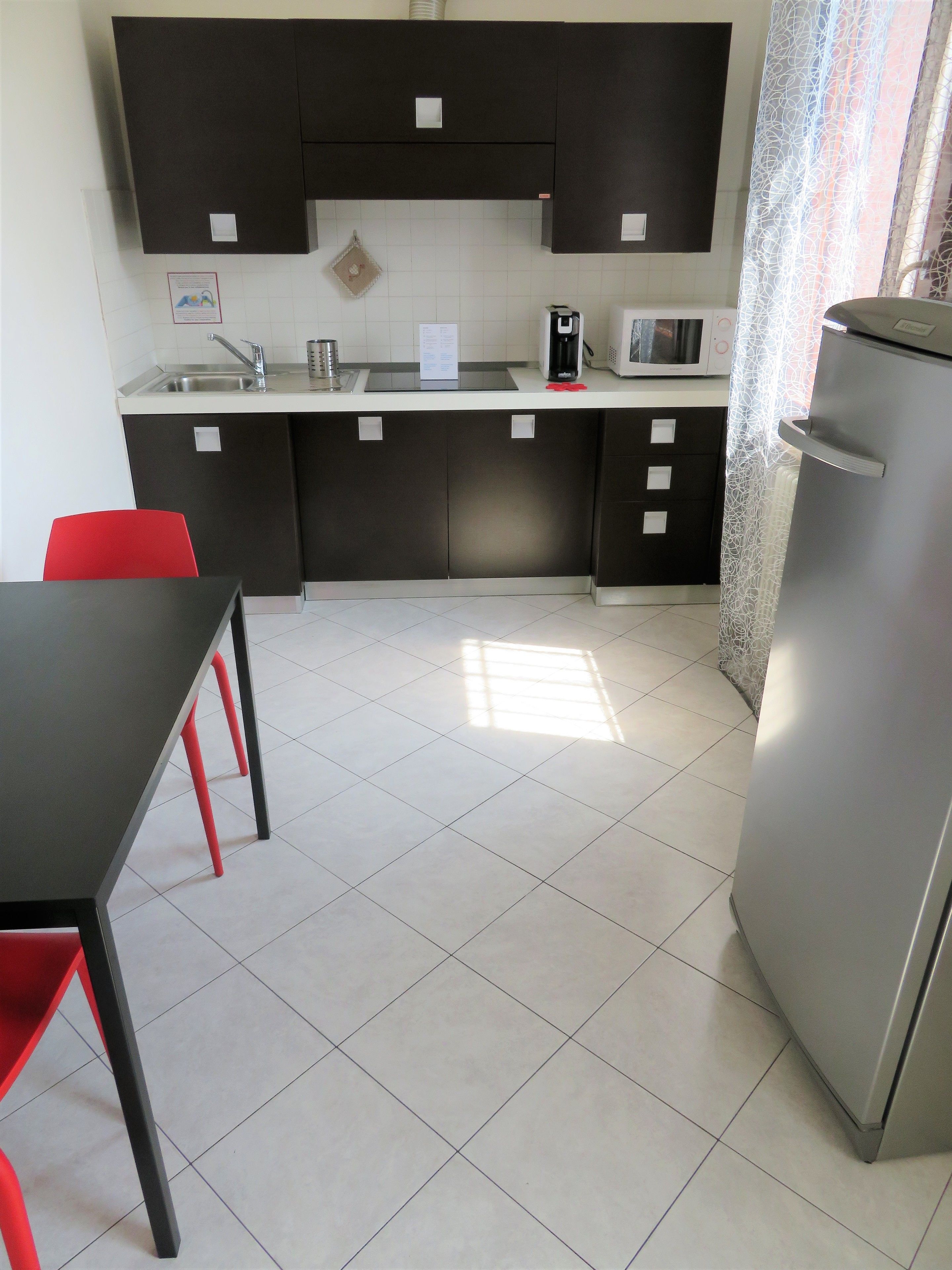 A modern kitchen with a dining area, featuring a refrigerator, microwave, and a sink.