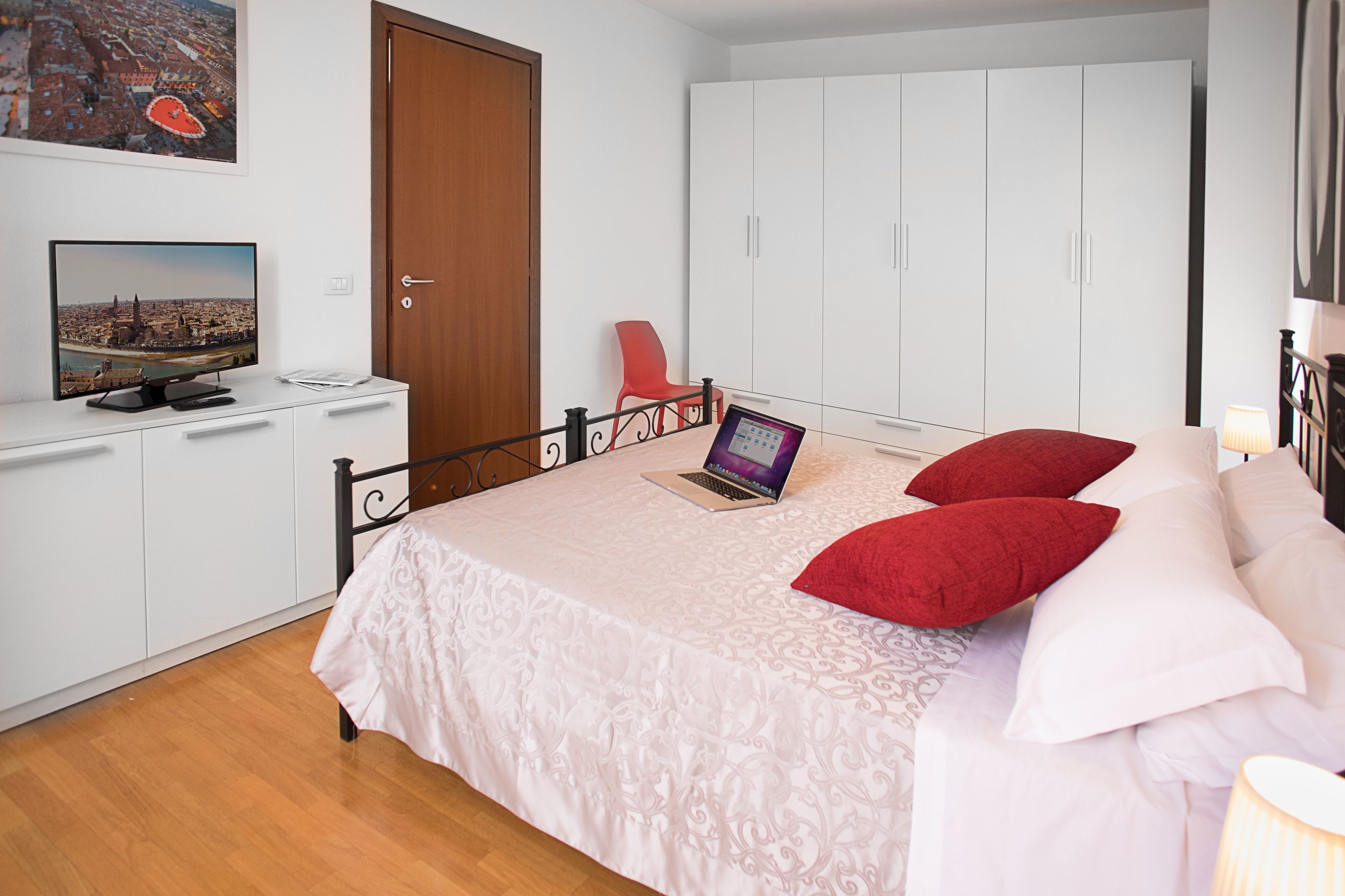 A bedroom with a bed, a laptop, a TV, and a wardrobe.