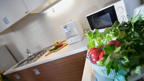 Una cocina con armarios blancos, microondas y una encimera con verduras frescas.