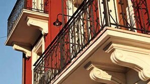 Fachada de edificio con balcón que presenta balaustradas blancas ornamentales y barandillas de hierro forjado negro.