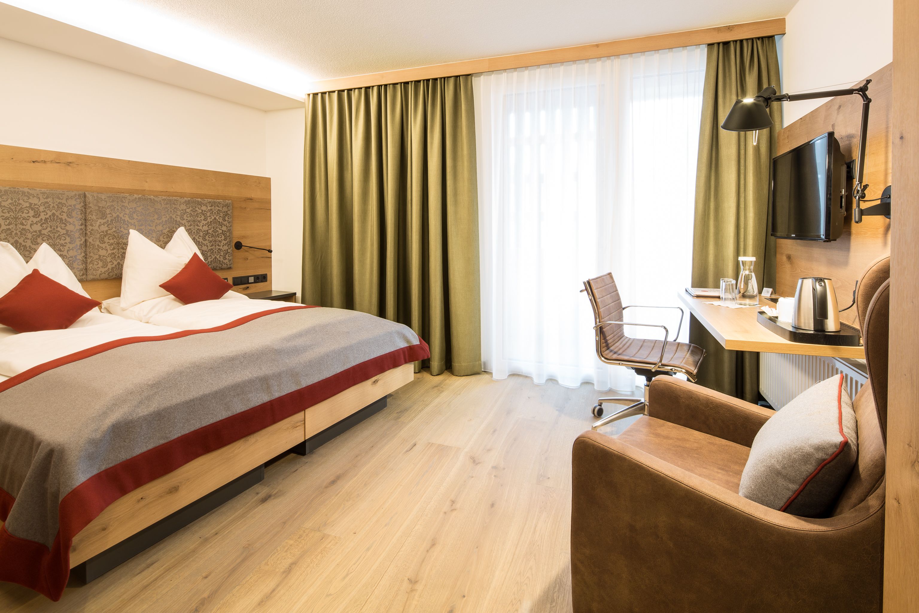 A hotel room with a bed, a desk, a chair, a TV, and a window with curtains.