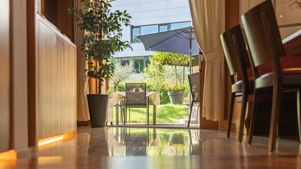 Un vestíbulo de hotel con piso reflectante, una planta en maceta, una mesa con sillas y un paraguas.