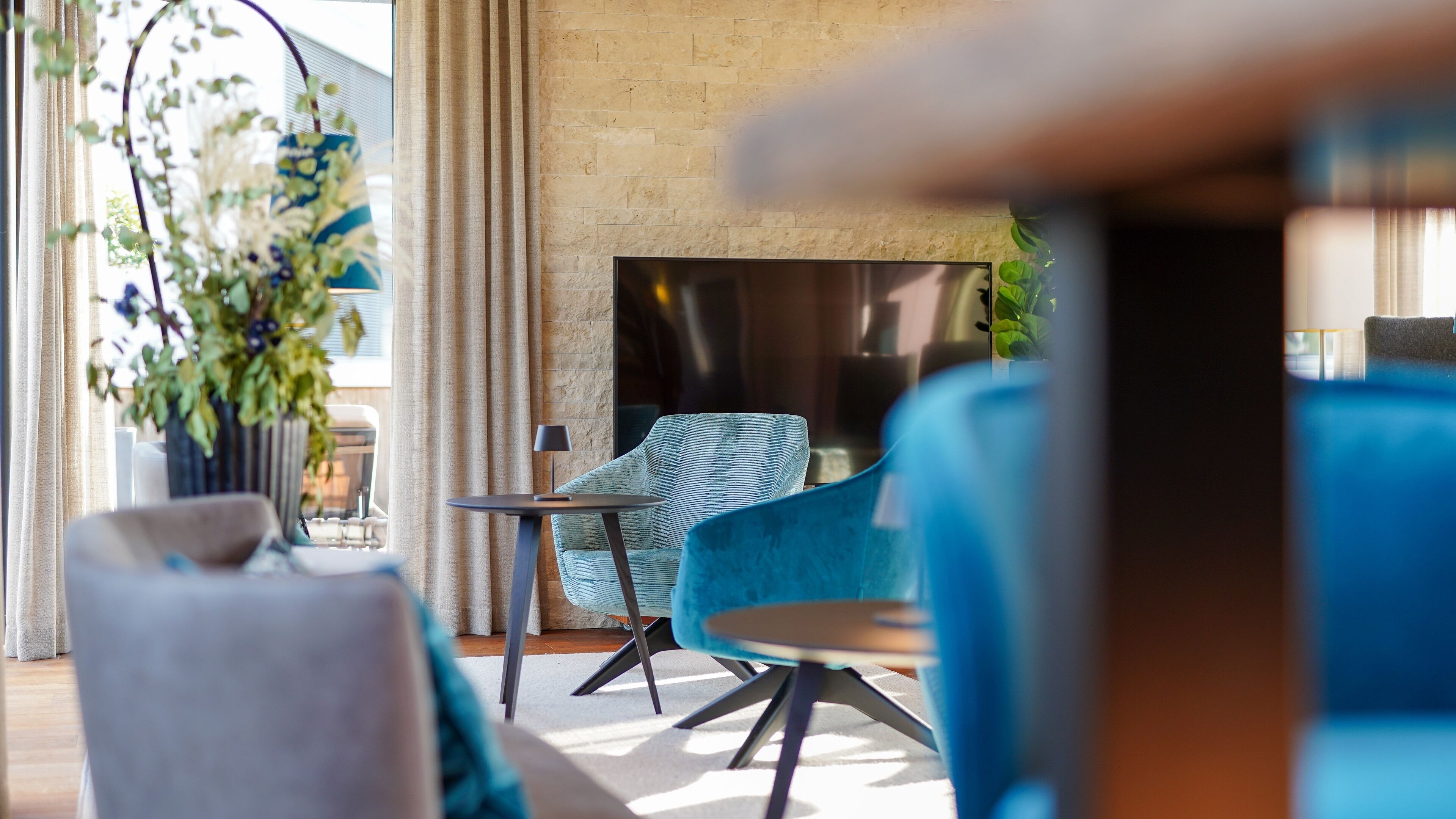 Un espace de détente moderne avec un mur en pierre, une cheminée et différents éléments de mobilier, notamment un fauteuil bleu et une petite table ronde.