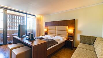 A hotel room with a bed, a desk with a computer, a chair, a sofa, and a window with curtains.