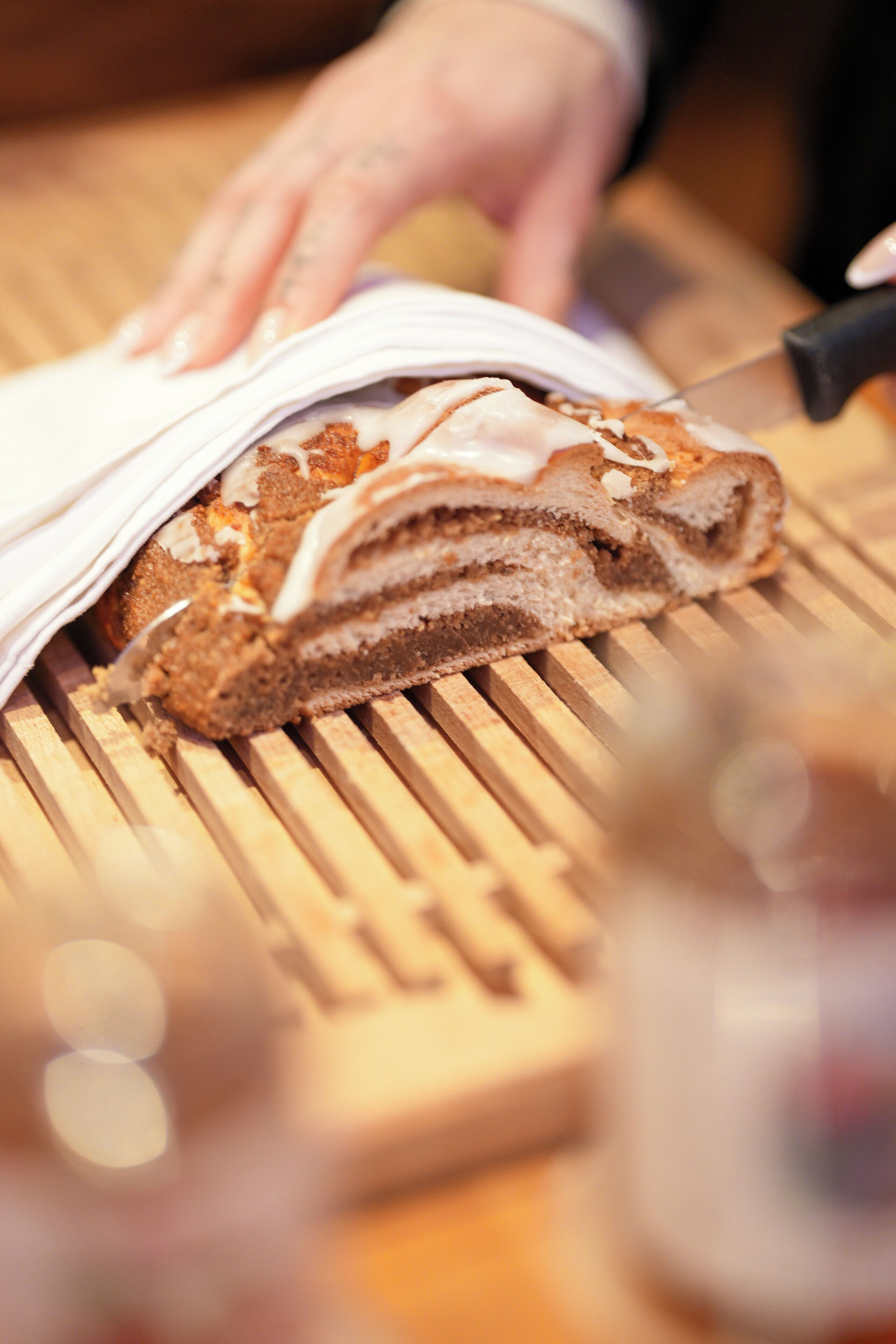 A close-up of a hand slicing a layered cake on a wooden cutting board.