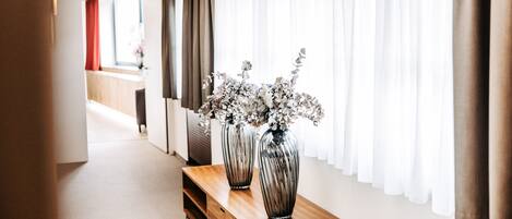 Un pasillo con un banco de madera, dos jarrones con flores y una ventana con cortinas blancas y translúcidas.