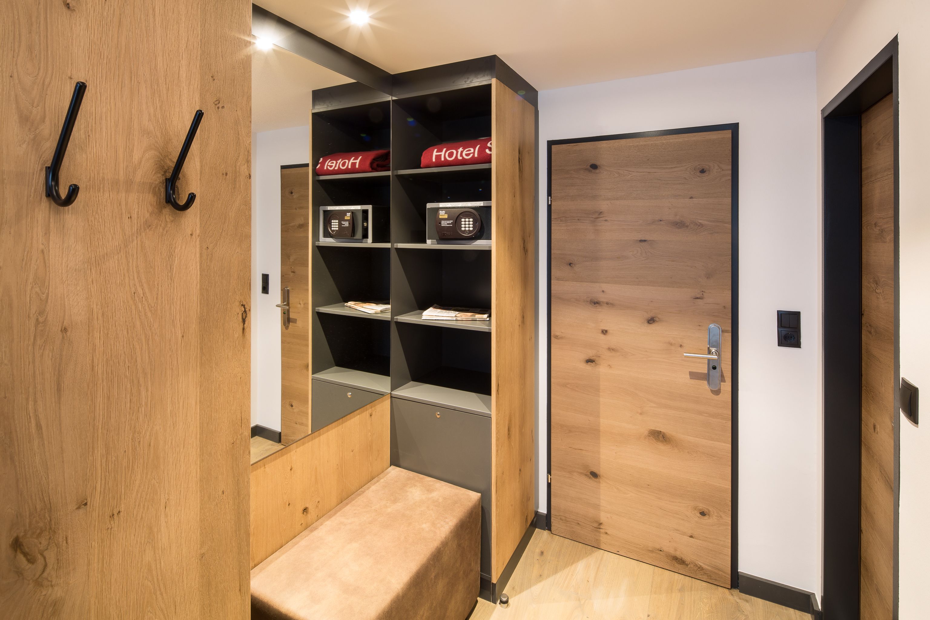 Ein modernes Hotelzimmer mit einer Holztür, einer eingebauten Bücherwand mit roter Beschilderung und einer Bank.