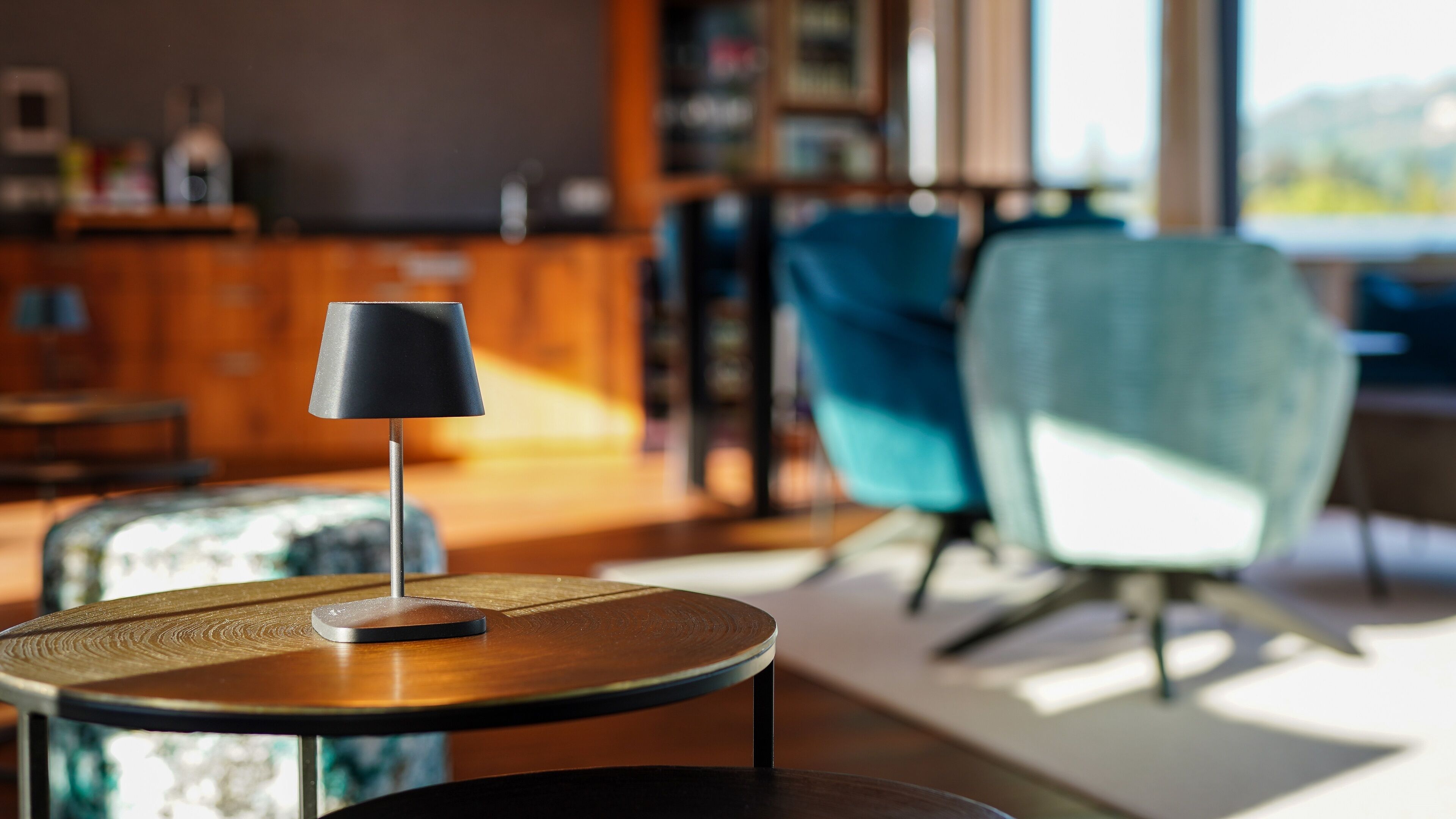 Uma sala de estar moderna com uma mesa de madeira redonda, um abajur preto e uma cadeira azul-turquesa.