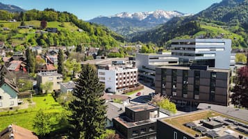 Ein modernes Hotel mit Dachgarten, umgeben von Wohnhäusern und Bergen.