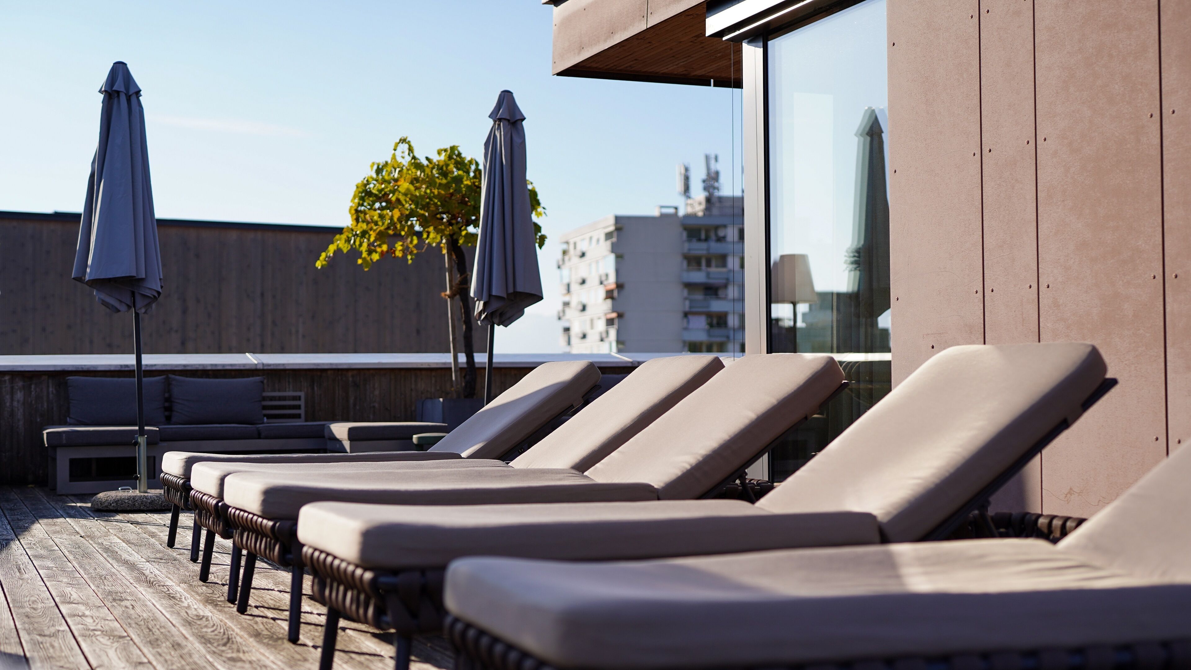 Un espace de détente aménagé sur le toit, avec des chaises longues et des parasols, une terrasse en bois et une vue sur les bâtiments en arrière-plan.
