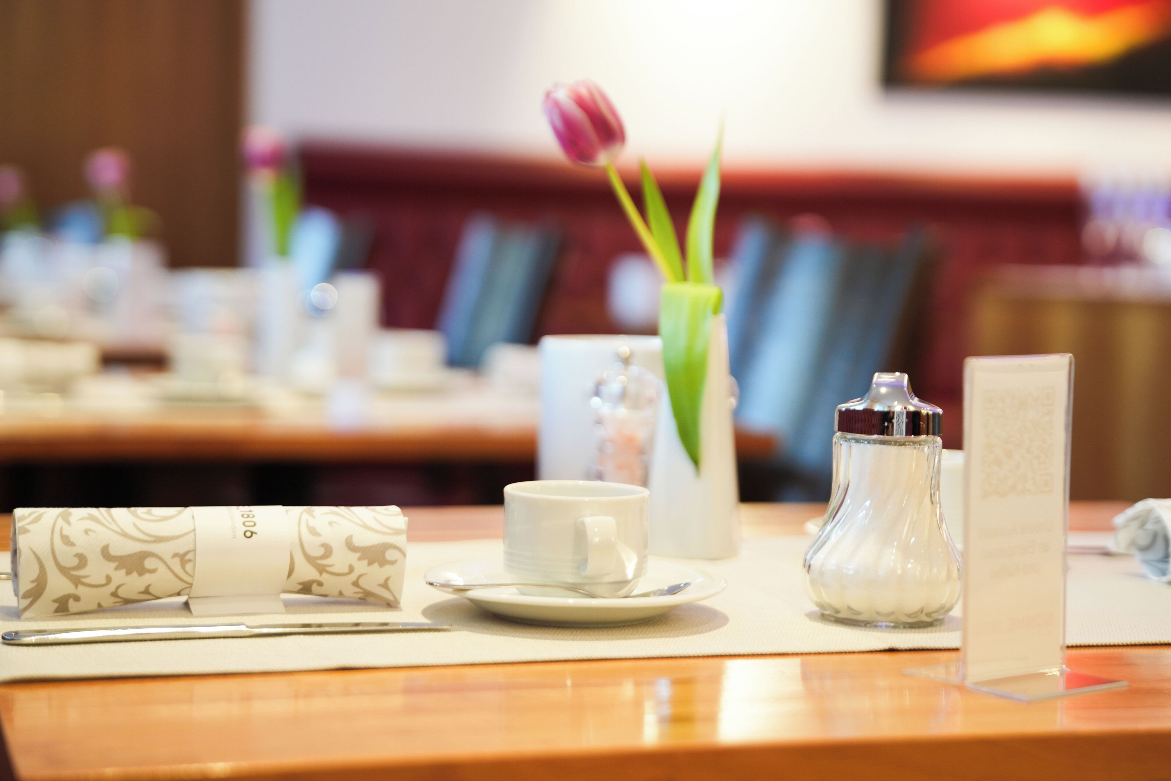 Una mesa de comedor con una taza blanca, un platillo y un mantel enrollado.
