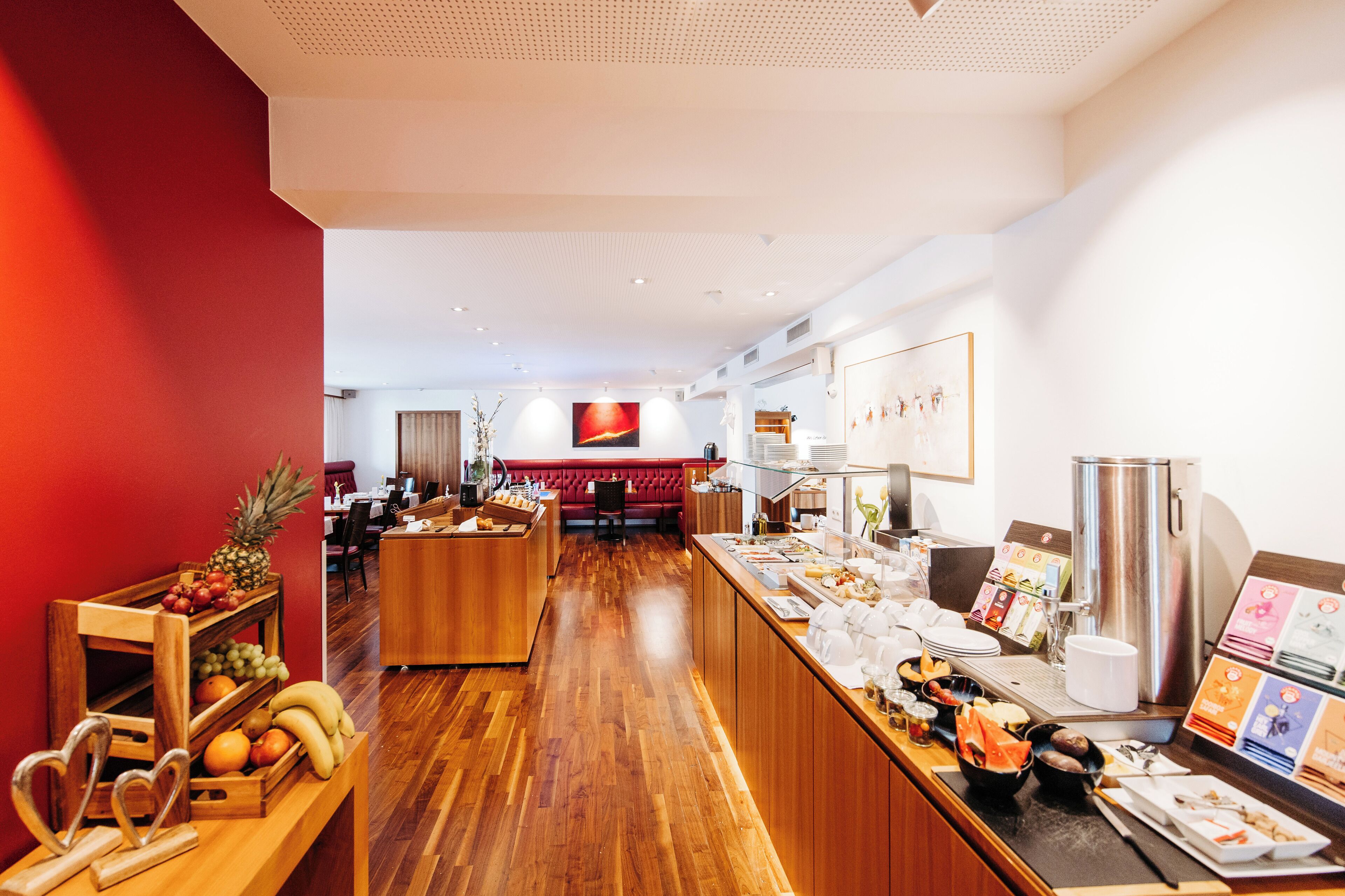 Un vestíbulo de hotel con un mostrador de recepción de madera, una exposición de frutas, una zona de estar y una pantalla grande.