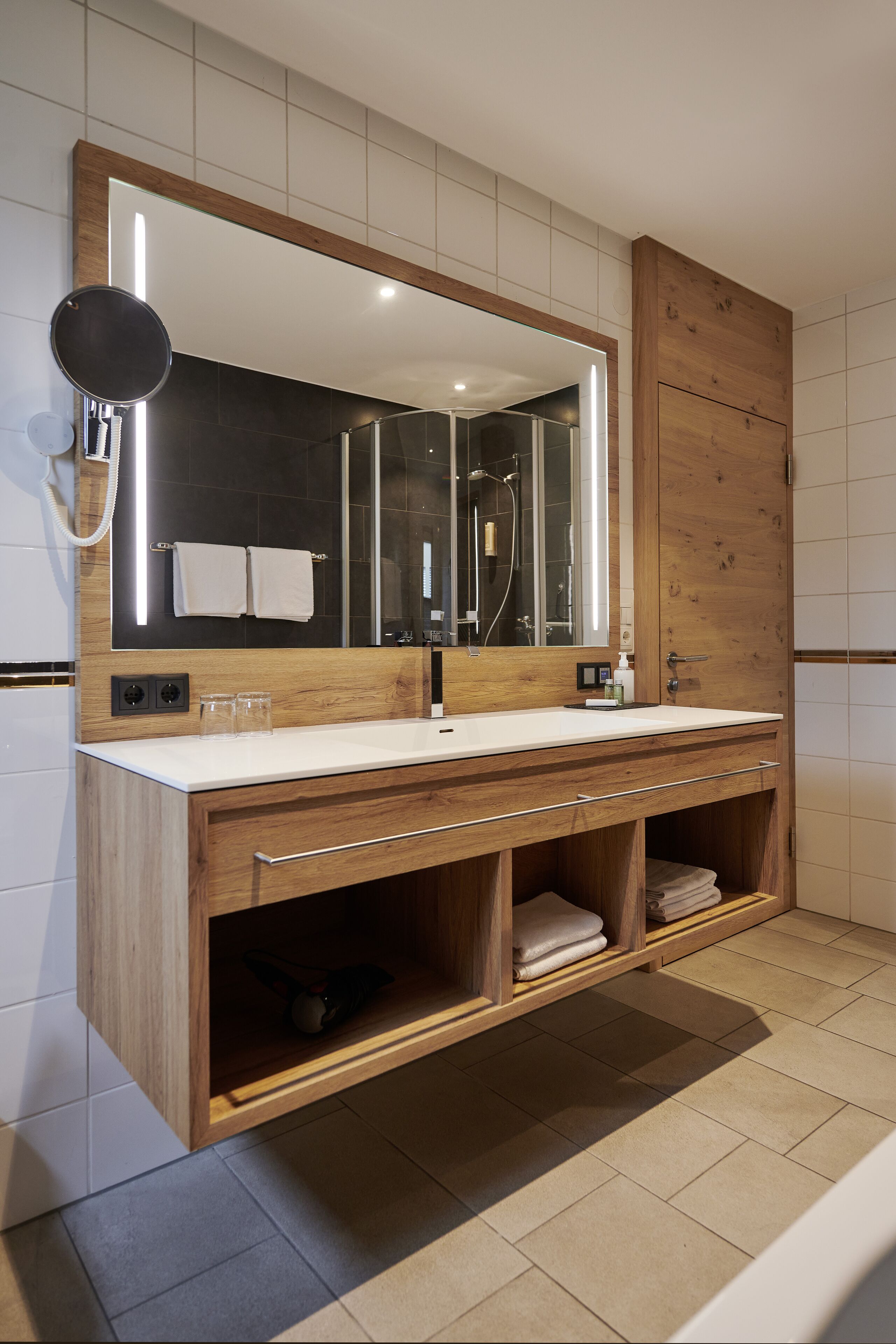 Ein modernes Badezimmer mit großem Spiegel, Holzwaschtisch und Duschbereich.